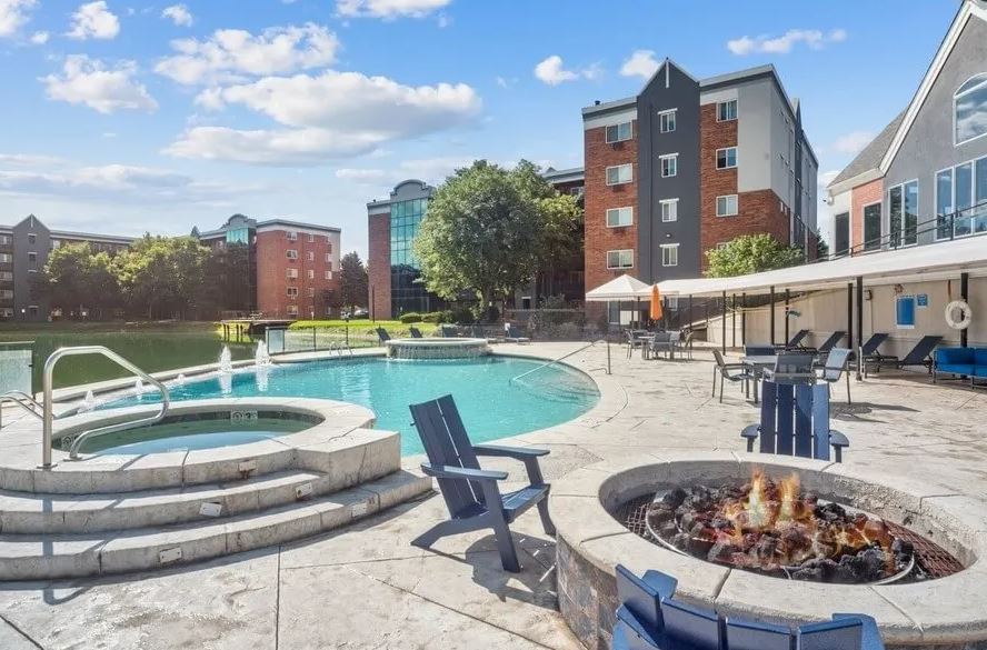 Outdoor pool area with hot tub, fire pit, lounge chairs, and tables at Esprit Cherry Creek, situated near apartment buildings under a partly cloudy sky.